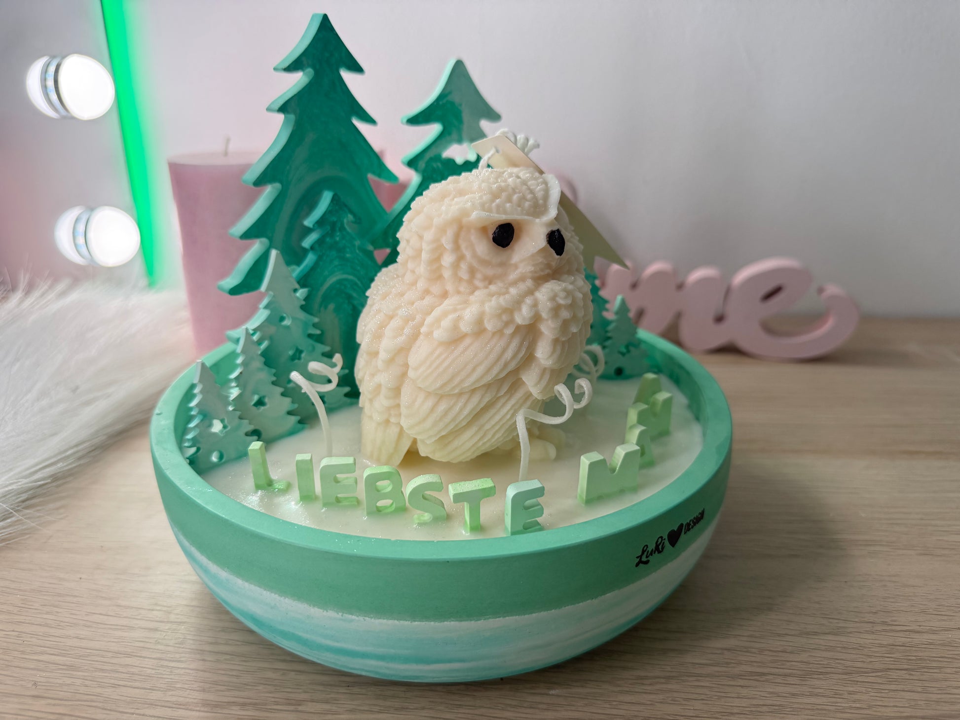 Detailaufnahme einer cremefarbenen Eulen-Kerze vor mintgrünen Gips-Tannenbäumen in einer handgegossenen Winter-Schale