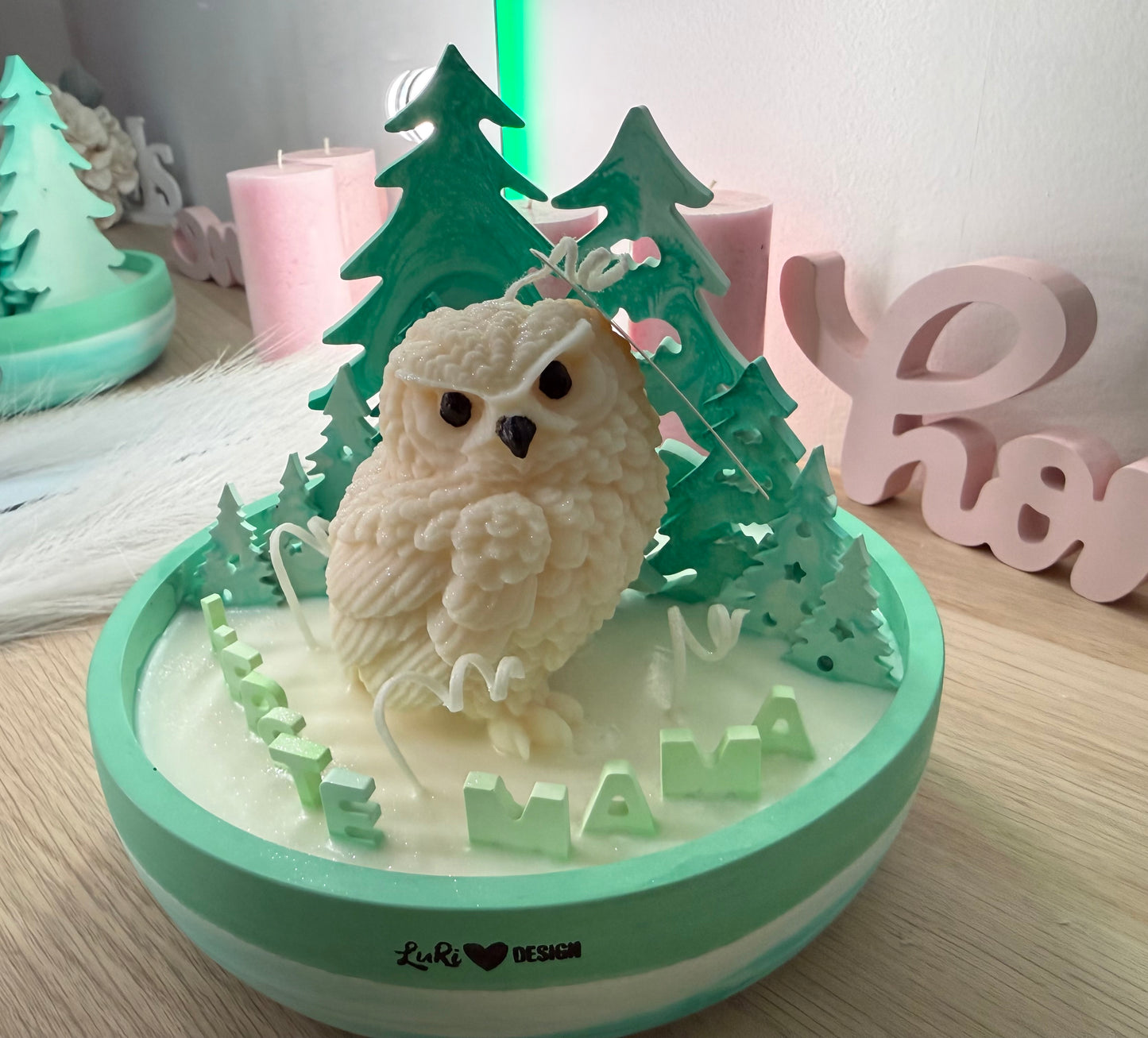 Winter-Schale von oben fotografiert: Eulen-Kerze aus Sojawachs, mintfarbener Gips-Wald und verteilte Deko-Elemente auf schimmernder Schneefläche.