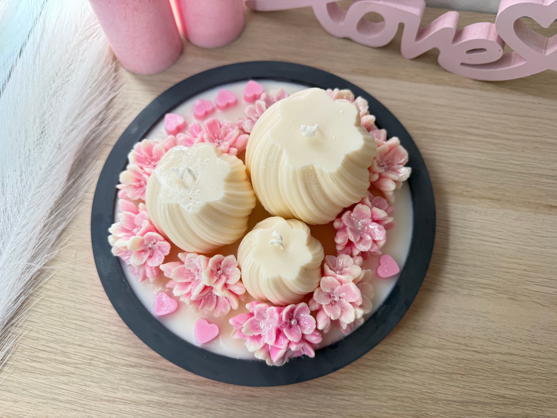Top-Ansicht einer handgemachten Kerzen-Deko-Schale mit drei Kerzen, umringt von fein gearbeiteten rosa Blüten und kleinen Herzen.